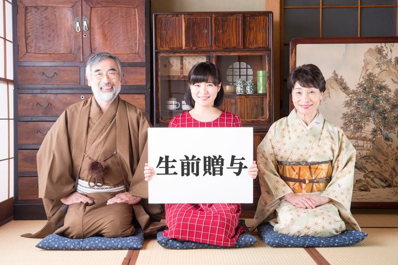 祖父母と孫娘が「生前贈与」のプラカードを持つ和室での記念写真